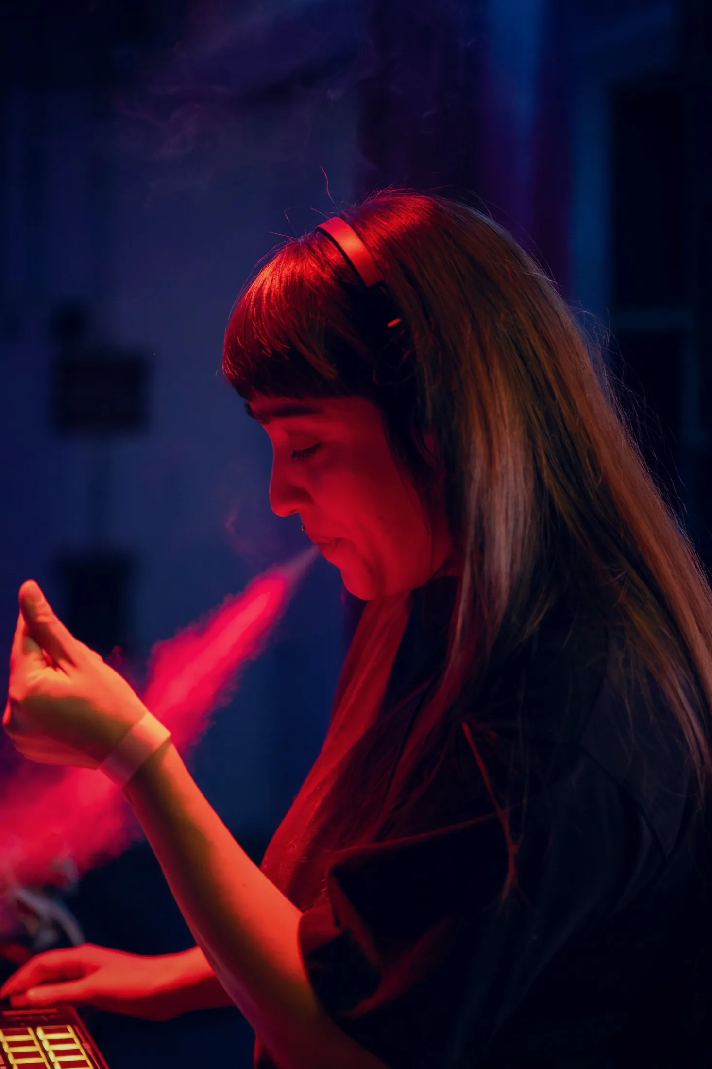 DJ con audífonos rodeada de humo y un haz de luz roja en plena mezcla — Ámbar por Libraphotos